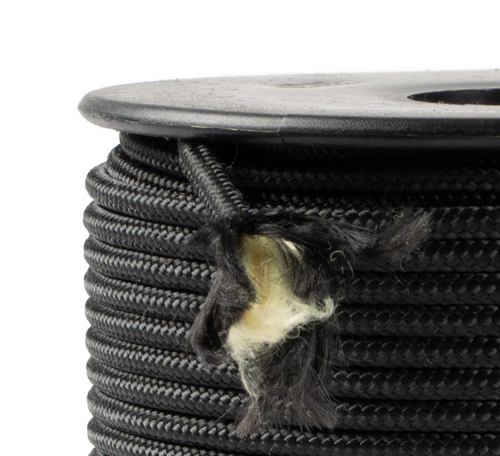Un gros plan d’un rouleau de corde Kevlar noire de 3 mm d’épaisseur, fabriquée à partir de fibres aramides avec une belle gaine en polyester, tressée de manière serrée et uniforme, dont une extrémité est effilochée et montre les fibres aramides beiges, enroulée sur une bobine noire avec des flasques rondes, sur un fond blanc.